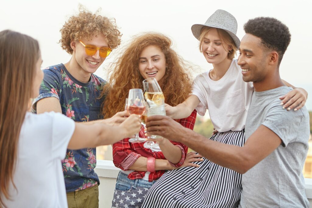 Five carefree happy friends clinking glasses of wine and cocktail with toast celebrating their succe