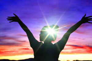 Mental health concept, Girl female holding her hands in the air at sunset with bright light on head.