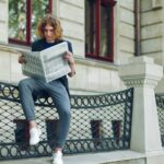 Young reddish man reading newspaper near old style building